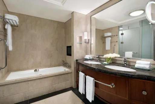 Bathroom with a built-in bathtub, stone tiling and a double vanity under a large mirror