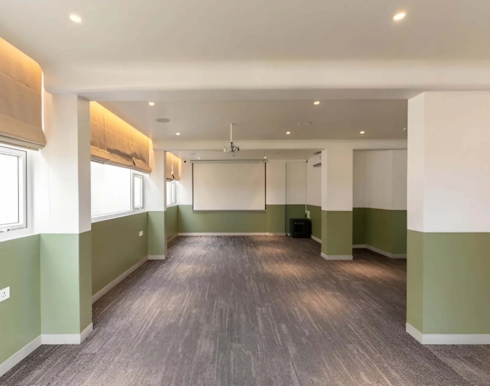 Large hall with green and white walls, grey carpet, recessed lighting and a projector screen
