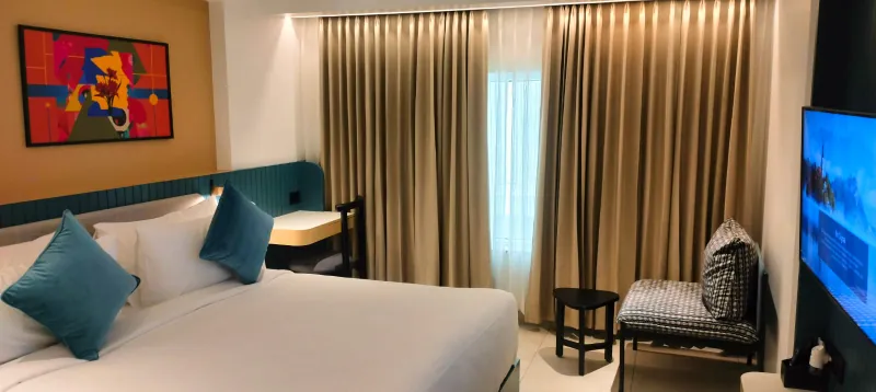Guest room with a teal headboard, blue cushions, bold artwork and gold curtains