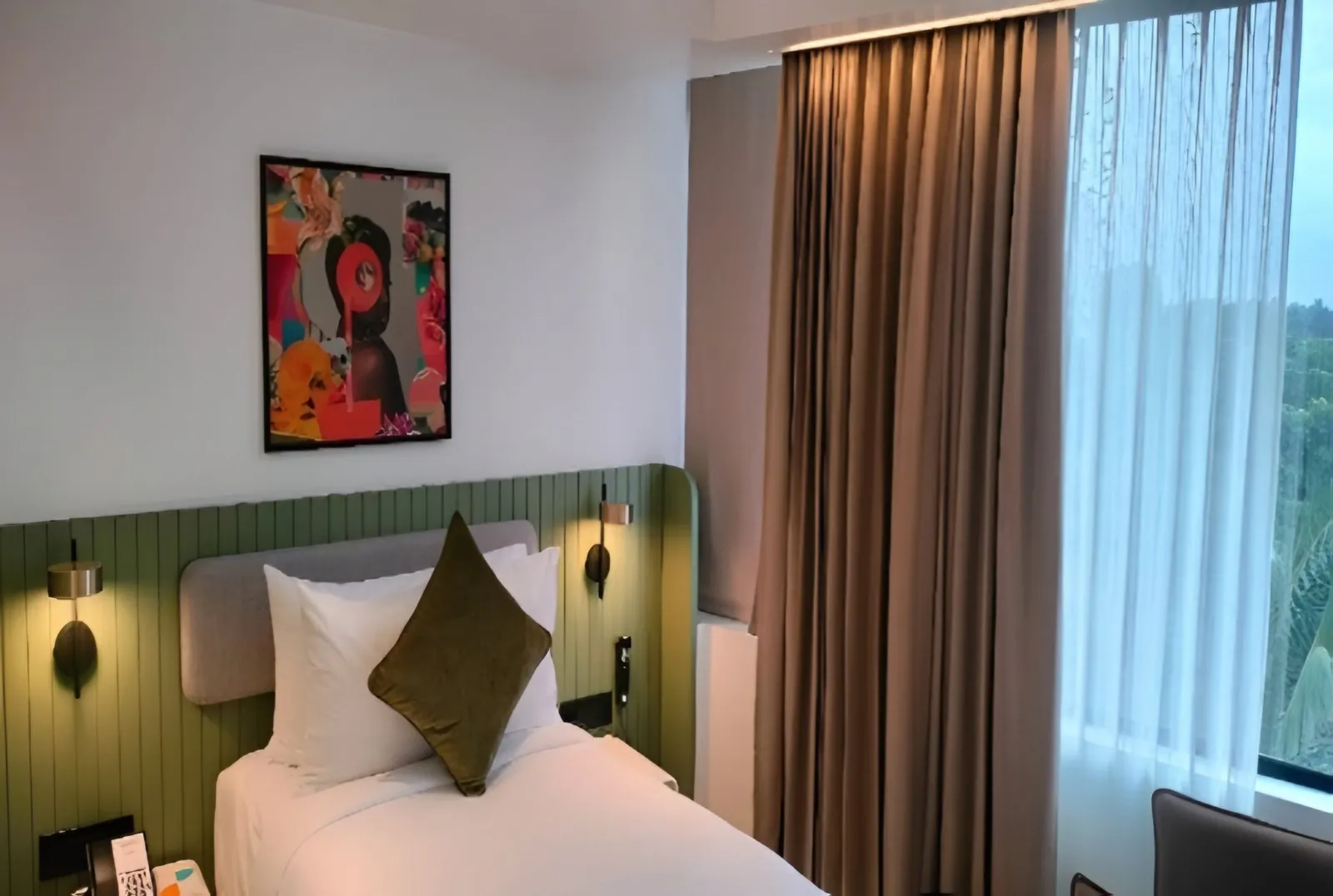 Single guest room with a green panelled headboard, wall lights and a framed artwork