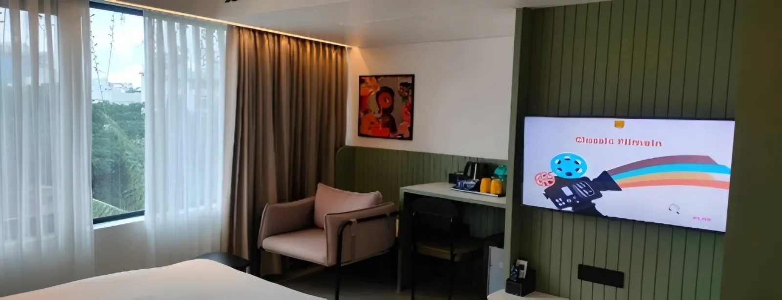 Guest room with a window, armchair, work desk and wall-mounted TV on green panelling