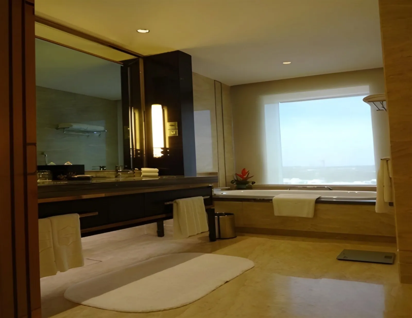Suite bathroom with a long vanity, a bathtub under a large window and a white bath mat