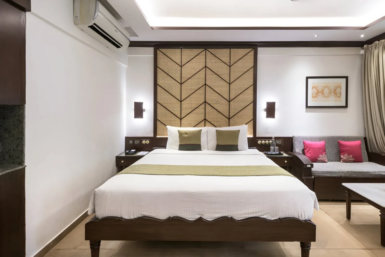 Renovated guest room with a woven chevron headboard, dark wood bed and a pink-cushioned sofa
